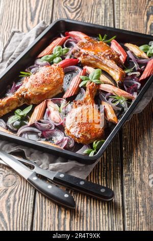 Baked honey pork chops with red onion and rhubarb close-up in a baking sheet on the table. Vertical Stock Photo