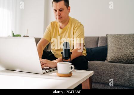IT freelancer men with microphone typing in laptop working from home office. Programmers sitting on couch doing code review. Distance learning online Stock Photo
