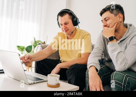 Two IT freelancer men typing in laptop working from home office. Two programmers sitting on couch doing code review. Distance learning online Stock Photo