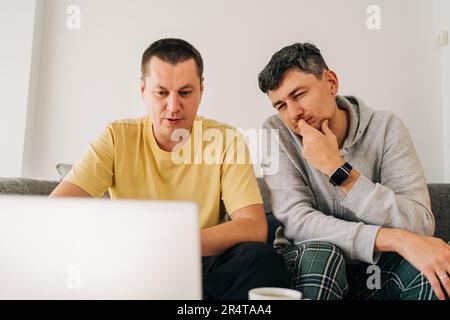 Two IT freelancer men typing in laptop working from home office. Two programmers sitting on couch doing code review. Distance learning online Stock Photo