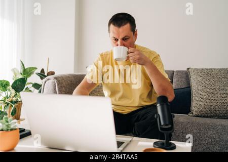 IT freelancer men with microphone typing in laptop working from home office. Programmers sitting on couch doing code review. Distance learning online Stock Photo