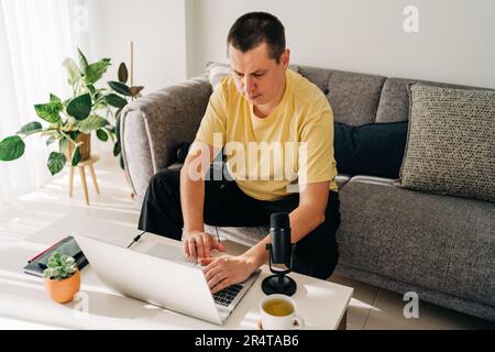 IT freelancer men with microphone typing in laptop working from home office. Programmers sitting on couch doing code review. Distance learning online Stock Photo