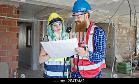 Man and woman builders reading house project speaking at construction site Stock Photo