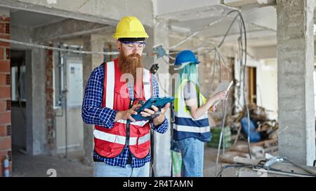 Man and woman builders using touchpad reading house project at construction site Stock Photo