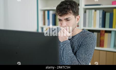 Young hispanic man using computer thinking at library university Stock Photo
