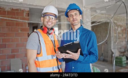 Two men builder and architect smiling confident writing document at construction site Stock Photo