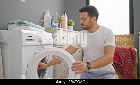 Young hispanic man doing laundry at laundry room Stock Photo