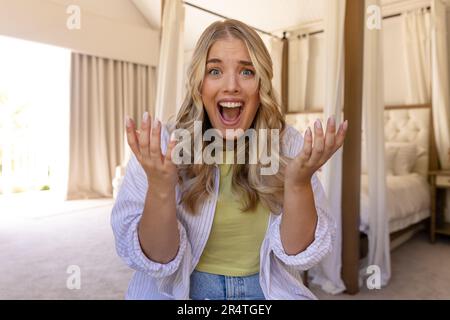 Surprised plus size caucasian young woman with mouth open looking at camera while sitting in bedroom Stock Photo