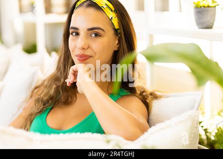 Close-up portrait of biracial young woman with hand on chin relaxing on sofa in living room Stock Photo