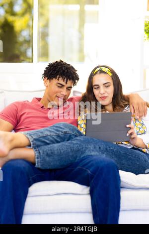Biracial young couple using digital tablet while relaxing on sofa in living room Stock Photo