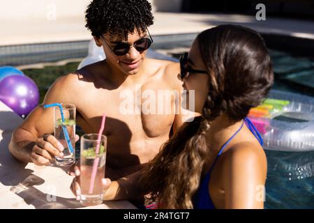 Biracial young couple wearing sunglasses with lemonade standing in swimming pool Stock Photo