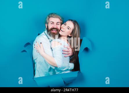Couple through hole in blue paper. Discount and sale, people hole background. Surprised couple of man and woman making hole in paper looking through Stock Photo