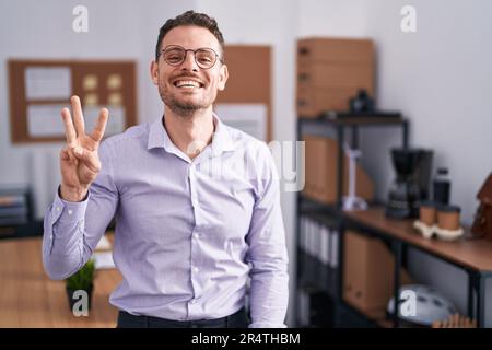 Young hispanic man at the office showing and pointing up with fingers number three while smiling confident and happy. Stock Photo