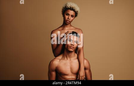 Young and empowered couple confidently looking at the camera in a monochrome studio shot; proudly owning their melanin-rich skin and muscular build. Stock Photo