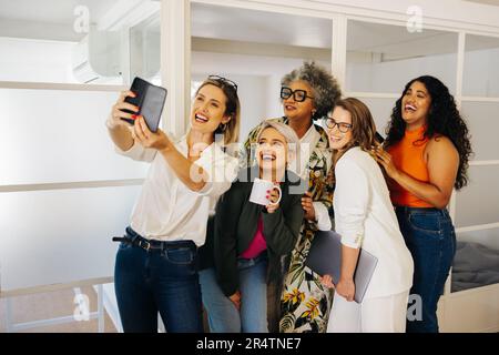 Diverse businesspeople smiling cheerfully while taking a selfie together in a creative office. Group of multicultural businesspeople celebrating their Stock Photo