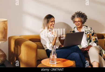 Cheerful businesswomen having a video call with their business partners in an office lobby. Two successful female entrepreneurs attending an online me Stock Photo