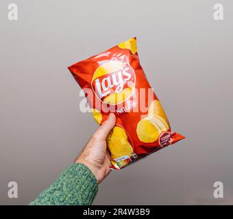 Lyon, France - May 24, 2023: A persons hand grasps a bright bag of Lays chips against an empty, gray background - delicious salt nature chips snack fo Stock Photo