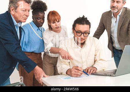 Multicultural team with seniors and juniors around developer's desk. They're discussing wireframes for mobile app or website. Stock Photo