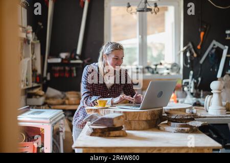 Female carpenter using laptop in a carpentry workshop Stock Photo