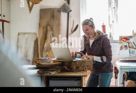 Female carpenter using laptop in a carpentry workshop Stock Photo