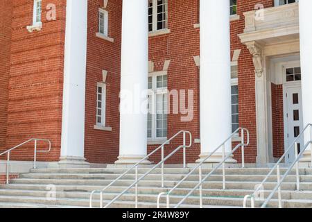 Four large white round columns at the facade entrance to a red vintage brick building. There are multiple panes of glass in tall white windows. Stock Photo