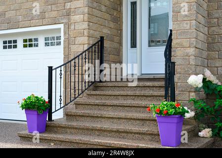 A large white garage door with small glass windows on a beige brick executive house with a white door and steps leading up to a grand entrance. Stock Photo