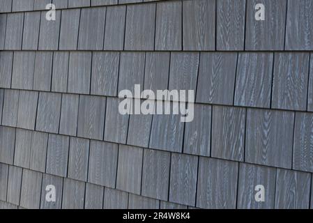 Natural grey cedar shake siding worn and textured on an exterior wall of a building. The thick rustic but smooth wood has faded in the sun. Stock Photo