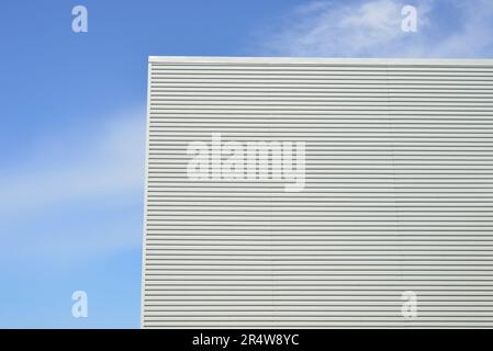 The exterior wall of a white commercial building. The metal horizontal siding with clean lines and corner boards against a blue sky with white clouds. Stock Photo