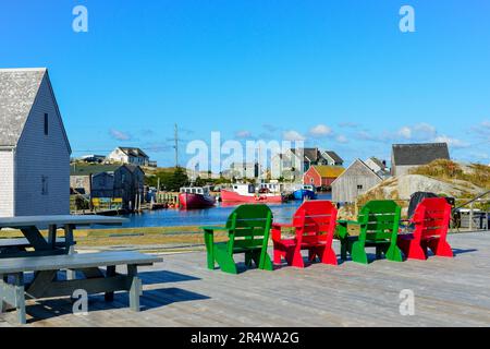 Red and green wooden chairs on a wharf in historic Lunenburg, Nova Scotia. The harbour is surrounded by vintage wooden fishing sheds and boats moored Stock Photo