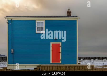 An exterior single traditional red wooden shutter door with cream color trim, black hinges, and vintage latch on a vibrant blue color exterior wall. Stock Photo