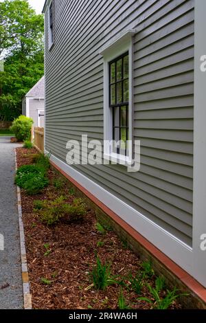 A double hung window with black wood frames, and multiple panes of glass, in a tan color wooden wall. The wall has narrow clapboard with white trim Stock Photo