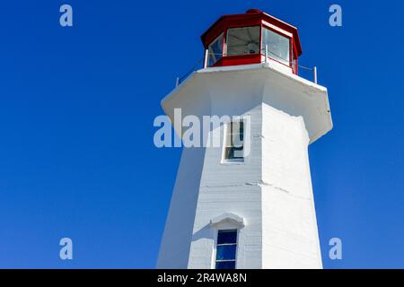 A vintage octagon shaped white concrete lighthouse with two small glass windows, a red metal watch tower with a green light, and a metal rail. Stock Photo