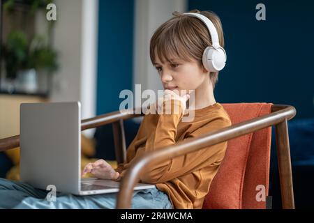 Interested child boy in headphones type on laptop enjoy internet education, play online video game Stock Photo