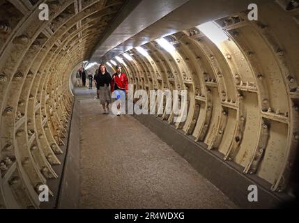 Interior of the Greenwich Foot Tunnel in London, showing pedestrians walking through the tiled underground passage beneath the River Thames Stock Photo