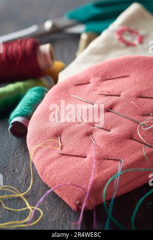 close-up of diy fabric needle holder or pin cushion with spool of threads on wooden table top, sewing tools in selective focus Stock Photo