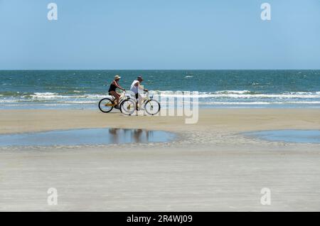 Sunny day on the beach on Hilton Head Island, South Carolina.  Visitors ride rented bicycles near the surf at low tide. Stock Photo