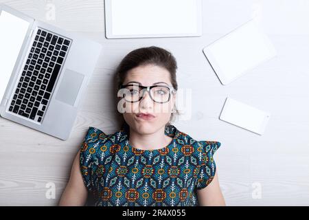 Doubtful expression on web writer surrounded by electronics. Her ideas seem used, AI outpaces her Stock Photo