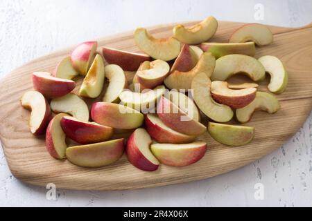 Wooden board with sliced apples for baking or other dishes on a light blue background. Stock Photo