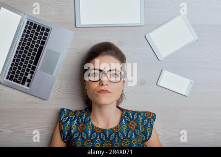 Surrounded by electronics, a web writer appears unsure. AI seems to have stolen her thunder Stock Photo