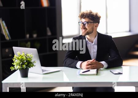 Software designer discussing a new project with his client on the phone. Creative business man working on a laptop in an open plan office. Stock Photo