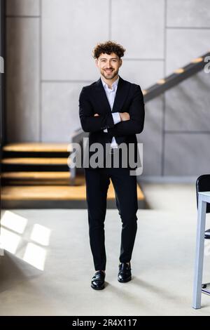 Successful businessman in formal wear standing with folded arms in modern coworking office and looking through window, thinking about startup, plannin Stock Photo