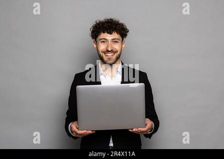 Smiling young unshaven business man isolated on grey wall background hold laptop pc computer Stock Photo