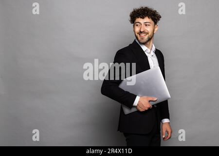 Smiling young unshaven business man isolated on grey wall background hold laptop pc computer Stock Photo