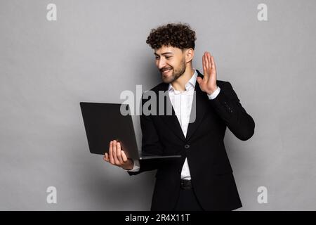 Man business stares at laptop and works thoughtfully online smiling over the internet in business suit video call business talks on gray background co Stock Photo