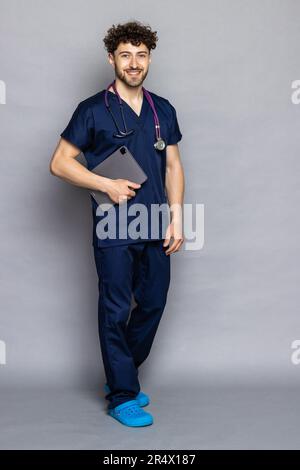 Portrait of young doctor holding tablet against grey background Stock Photo