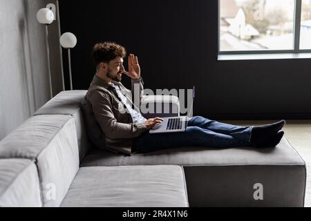 Young man is browsing at his laptop and calling with customer on the sofa at home, Business success Stock Photo