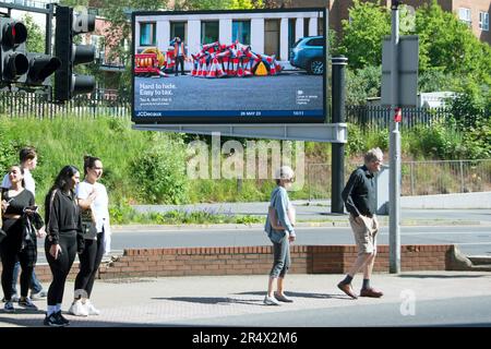 pedestrians wait at a crossing in kingston, surrey, england, in front of a digital billboard from the dvla warning of avoiding vehicle tax Stock Photo