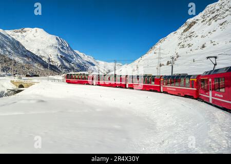 Grisons, Switzerland - November 05. 2021: The famous red Bernina Express tourist train is crossing the snow field in the Alps height. Stock Photo