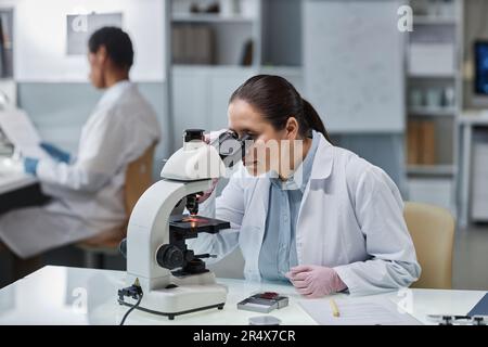 Portrait of young woman scientist looking in microscope while doing research in laboratory, copy space Stock Photo