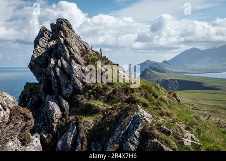 Close-up of a rocky, sea cliff outlook with a distant view from Sybil Head of the Three Sisters mountain peaks along the Atlantic Coast on Dingle P... Stock Photo
